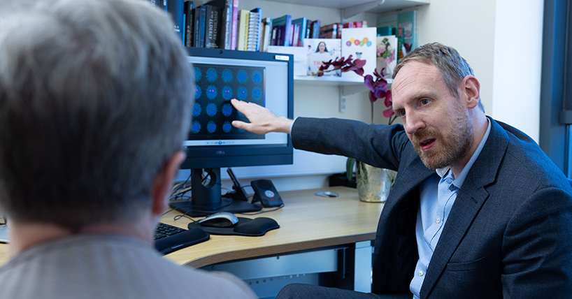 Prof Taylor points to computer screen which has lots of brain scans displayed